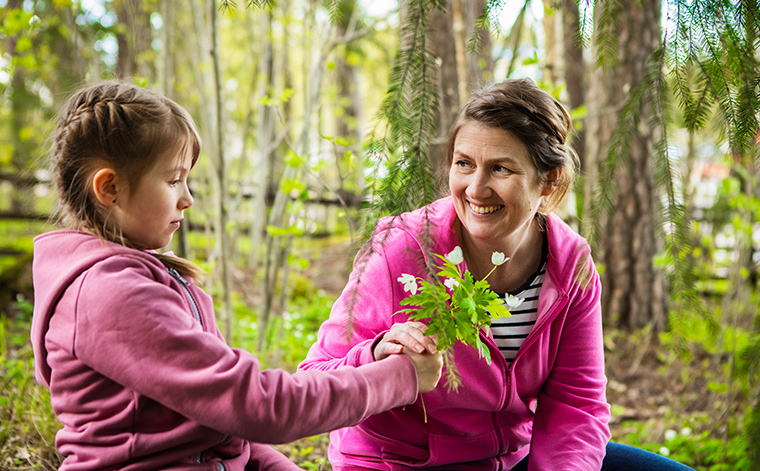Tytär ojentaa metsässä kukkia Kirsi Somervuolle.